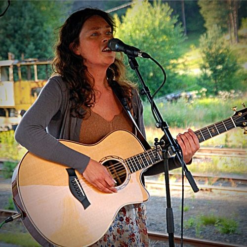 Viil is singing and playing the guitar at a concert outside. 